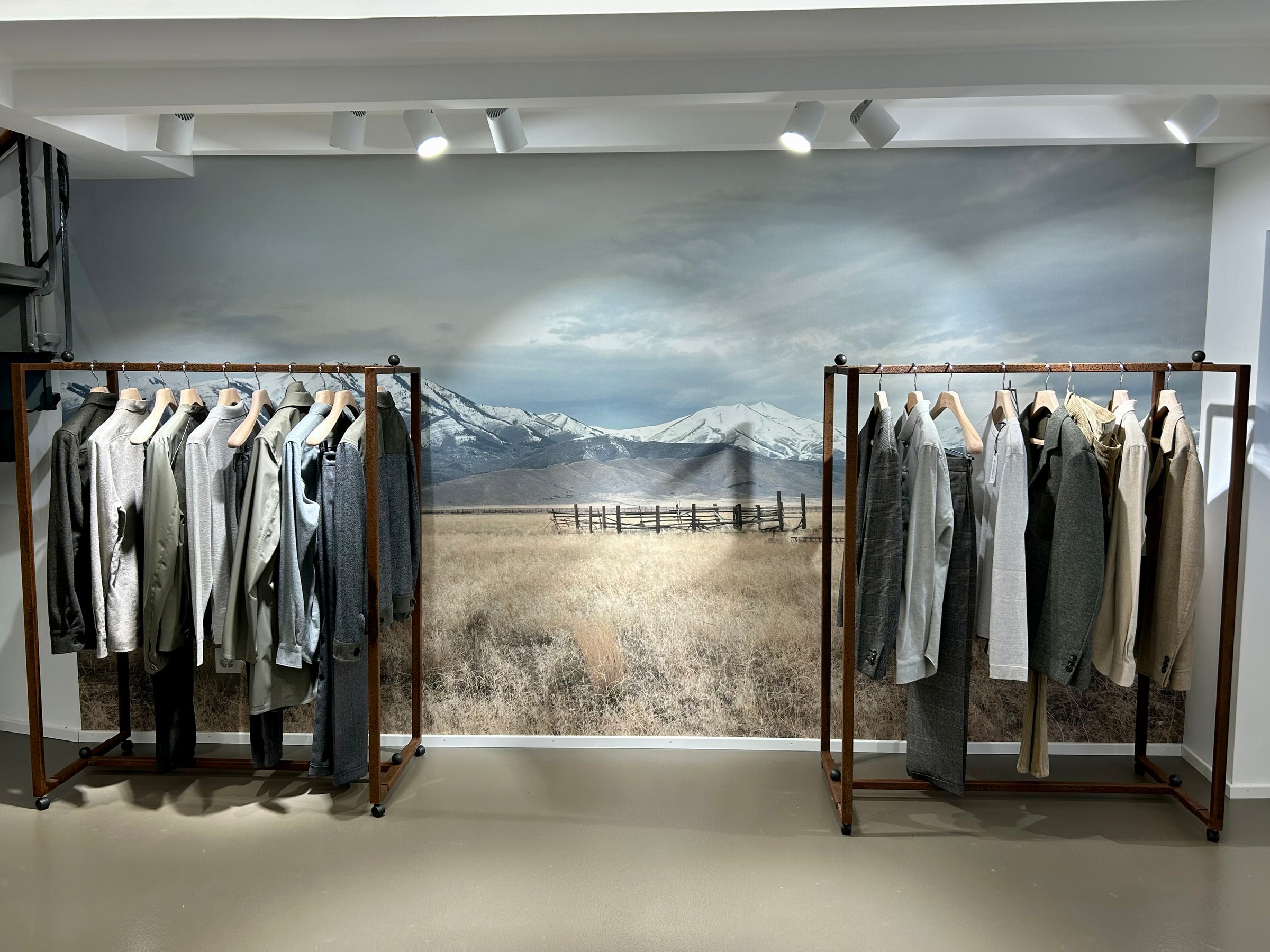 Interior of the KA/NOA menswear store in Lausanne featuring two clothing racks with various gray and beige men's garments