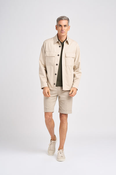 Male model wearing a stylish KA/NOA beige jacket and matching beige shorts, paired with a dark green shirt and light sneakers, showcasing modern casual fashion for men.