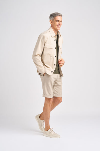 A man in a beige Norat jacket in Trofeo cotton and wool, olive shirt, and matching shorts, complemented by beige sneakers against a plain background.