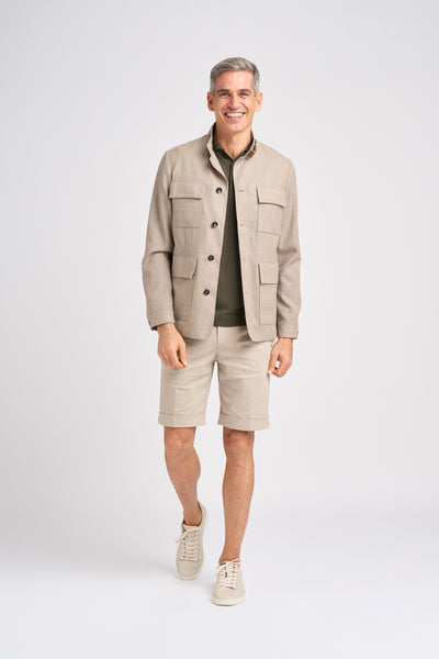 A man wears a beige wool jacket over an olive shirt, paired with light shorts and sneakers.
